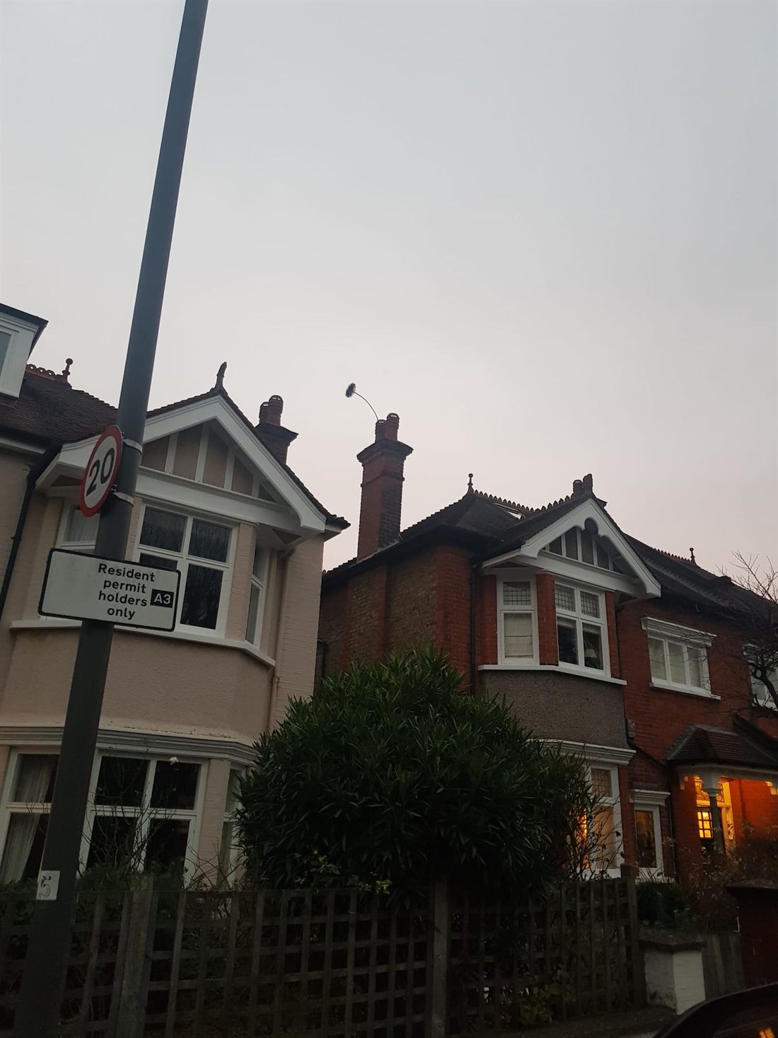 A sweeping brush showing above the chimney pot at dusk, the traditional sign the flue is clear